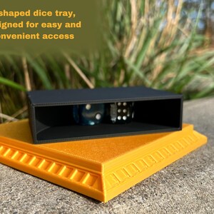 May include: A black U-shaped dice tray with a raised base. The tray is designed for easy and convenient access to dice. The tray is sitting on a yellow base with a decorative border.