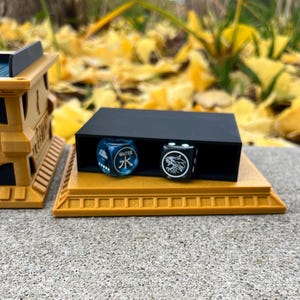 May include: A black dice tray with two dice, one blue with the Chinese character for water and the other black with a white wolf design, sits on a gold-colored base.