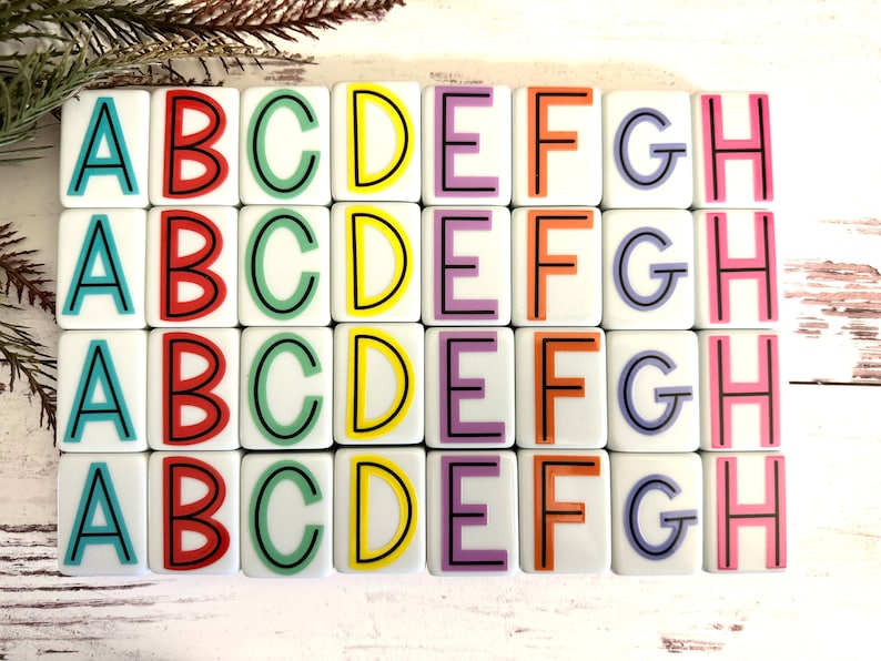 May include: A set of 32 white square tiles with the letters A through H printed on them in different colors. The letters are outlined in black. The tiles are arranged in four rows of eight tiles.