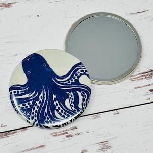 May include: A compact mirror with a white background and a blue octopus design. The mirror is round and has a silver trim.