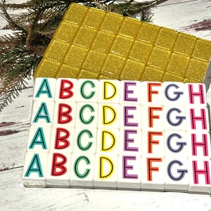 May include: A set of colorful alphabet tiles with letters A through H. Each tile is white with a black outline and a different color for each letter. The tiles are arranged in four rows of eight tiles.