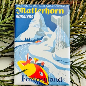 May include: A vintage-style illustration of the Matterhorn mountain with a bobsled racing down the snowy slopes. The text "Race thru alpine passes and ice caverns in Matterhorn Bobsleds" is at the top of the image. The text "Fantasyland" is at the bottom of the image.