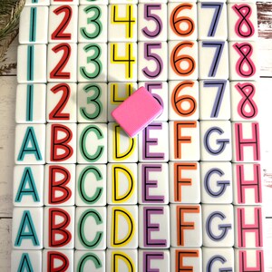 May include: A set of 36 white tiles with colorful numbers and letters. The tiles are arranged in four rows of nine. The numbers are 1 through 8 and the letters are A through H. The tiles are on a white wooden surface.