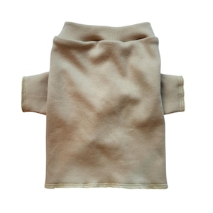 May include: A tan-colored pet sweater with a mock neck and short sleeves. The sweater is made of a soft, knit fabric and has a finished hem and sleeve cuffs. The garment is designed to fit a small dog or cat.