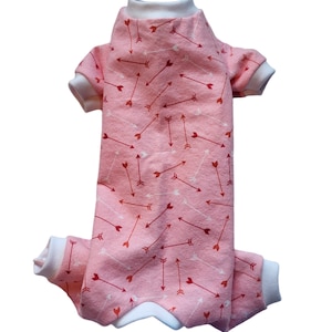May include: Pink dog pajamas with a white trim and a pattern of red and white arrows.