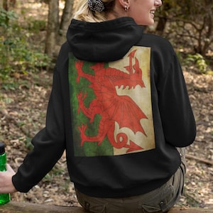 May include: Black hooded sweatshirt featuring a large red dragon design on the back, set against a green and white background. The dragon is a prominent symbol of Wales. The sweatshirt is a comfortable, casual garment.