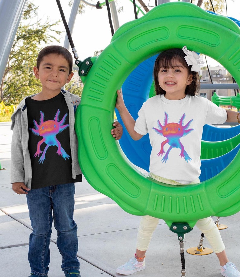 May include: Two children wearing t-shirts with a colorful axolotl graphic. The boy is wearing a black t-shirt and the girl is wearing a white t-shirt. They are playing on a green and blue playground swing set.