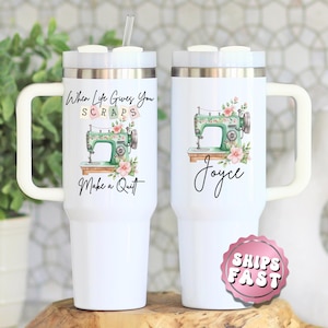 May include: Two white travel mugs with handles, each featuring a sewing machine design. One mug has the text "When Life Gives You Scraps, Make a Quilt." The other mug has the name "Joyce." Both mugs have a straw and a silver rim.