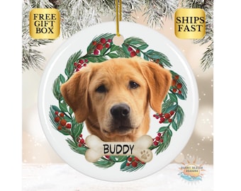 May include: A white ceramic Christmas ornament featuring a golden retriever dog with a red and green holly wreath around it. The dog's name, "Buddy", is written on a bone-shaped tag.