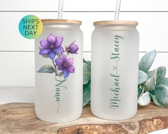 May include: Two frosted glass tumblers with bamboo lids and clear straws. One tumbler has a purple floral design and the name "Mama" written in cursive. The other tumbler has the names "Michael & Stacey" written in cursive.