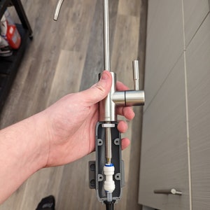 May include: A disassembled stainless steel kitchen faucet with a white filter and a gray plastic housing. The faucet has a curved spout and a lever handle.