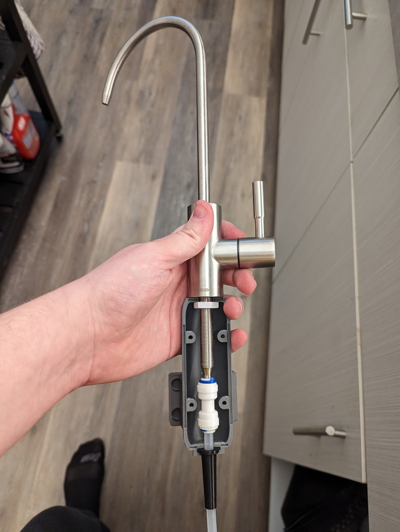 May include: A disassembled stainless steel kitchen faucet with a white filter and a gray plastic housing. The faucet has a curved spout and a lever handle.