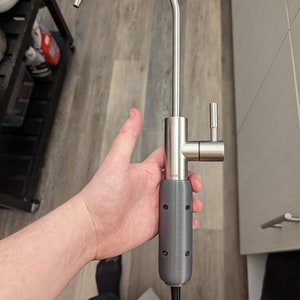 May include: A stainless steel kitchen faucet with a gray plastic handle and a white hose. The faucet has a single handle and a spout that is curved upwards.