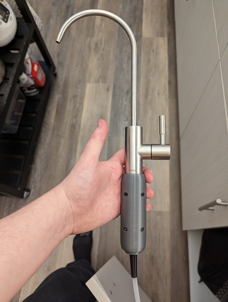 May include: A stainless steel kitchen faucet with a gray plastic handle and a white hose. The faucet has a single handle and a spout that is curved upwards.