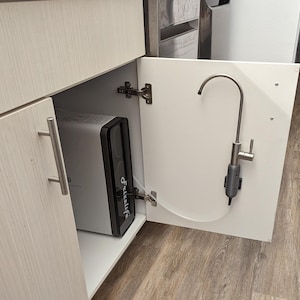 May include: A white cabinet with a silver faucet and a water filtration system inside. The system is a white rectangular box with a black front panel that says "Frizzlife".