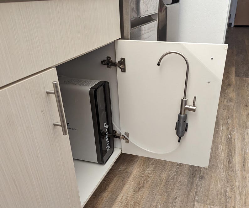May include: A white cabinet with a silver faucet and a water filtration system inside. The system is a white rectangular box with a black front panel that says "Frizzlife".