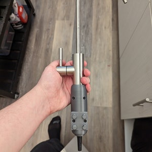 May include: A stainless steel kitchen faucet with a gray plastic adapter. The faucet has a single handle and a curved spout.