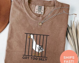 May include: A brown t-shirt with a white goose in a cage and the text "GOT TOO SILLY". The shirt is made of a soft, comfortable material and has a distressed look. The text "COLOR: ESPRESSO" is at the bottom of the image.