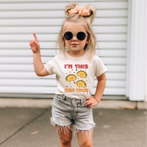 a little girl wearing sunglasses and a t - shirt that says i'm this