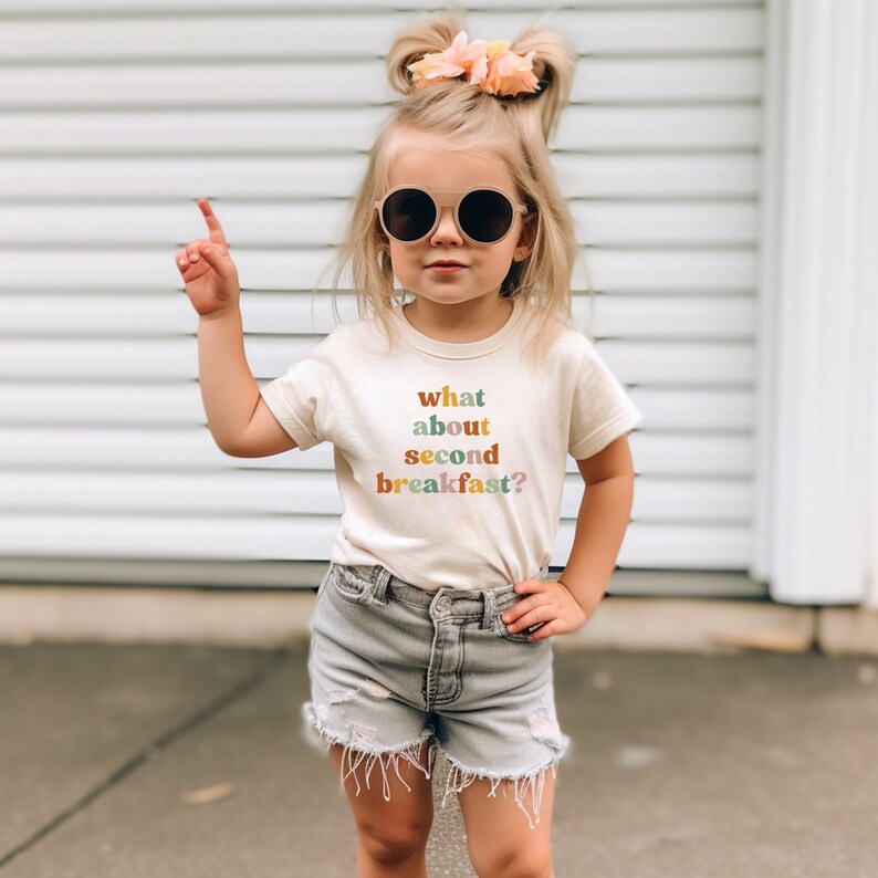 a little girl wearing a t - shirt that says what about second breakfast?