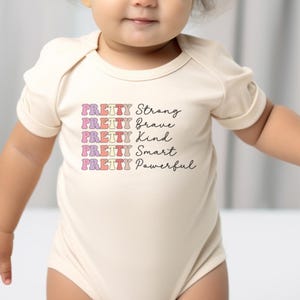 a baby girl wearing a bodysuit with words on it
