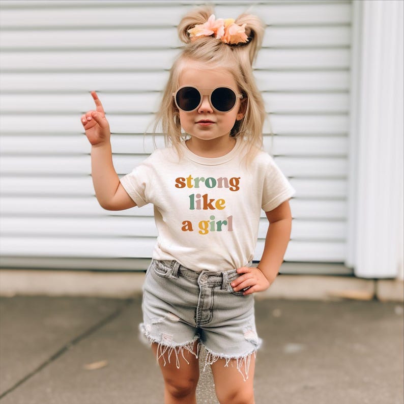 a little girl wearing a t - shirt that says strong like a girl