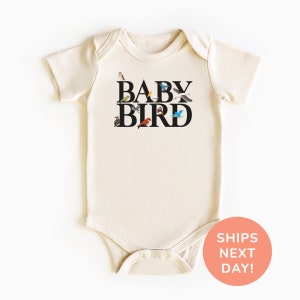 May include: A cream-colored baby onesie with short sleeves and a black graphic that says "BABY BIRD" with a variety of colorful birds surrounding the letters.