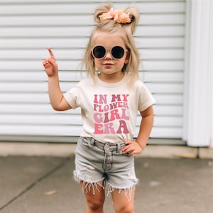 a little girl wearing a t - shirt that says i'm my flower girl