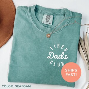 a t - shirt that says tired dad's club sits next to a hat