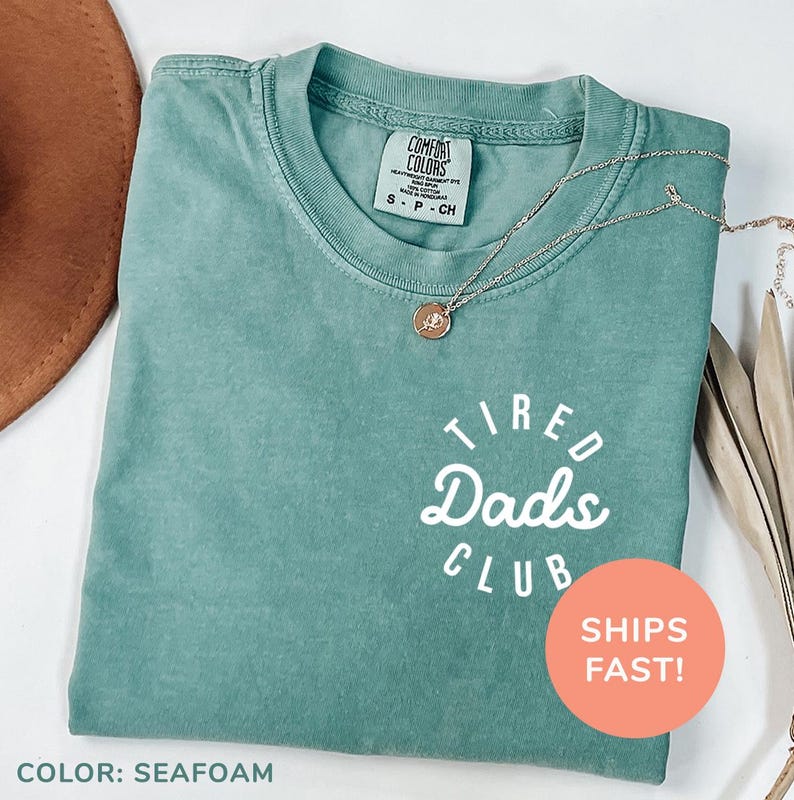 a t - shirt that says tired dad's club sits next to a hat