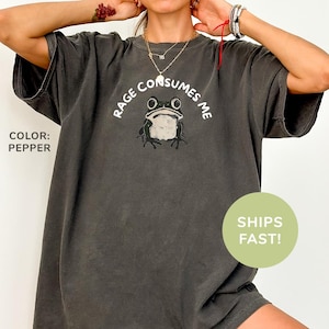 May include: A dark gray t-shirt with a frog graphic and the text "Rage Consumes Me".