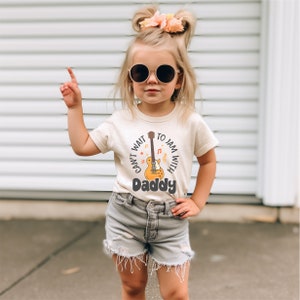 a little girl wearing a t - shirt with a guitar on it