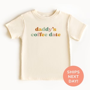 Peut inclure: Un t-shirt à manches courtes de couleur crème avec le texte "daddy's coffee date" en lettres colorées.
