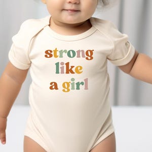a baby wearing a bodysuit that says strong like a girl