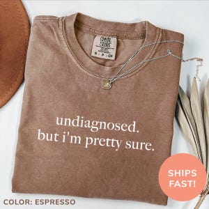 May include: A brown t-shirt with the text "undiagnosed. but i'm pretty sure." printed in white. The shirt is made of a soft, comfortable material.