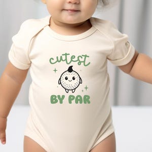 A baby wearing a white onesie with a cartoon character and text printed on it.