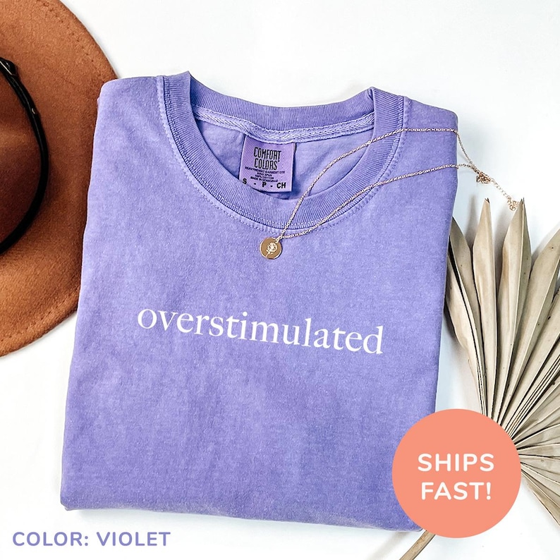 a t - shirt that says oversimulated on it next to a hat and