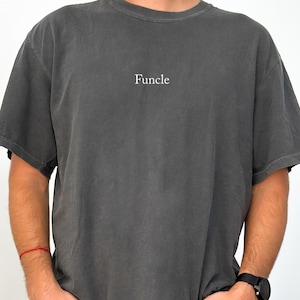 May include: A charcoal gray t-shirt with the word "Funcle" printed in white on the front.