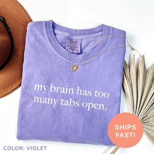 a purple shirt that says, my brain has too many tabs open