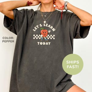 a woman wearing a gray shirt with a red apple on it