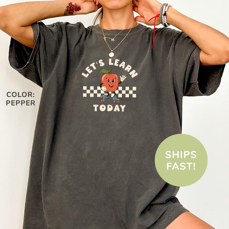 a woman wearing a gray shirt with a red apple on it
