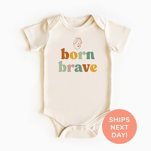 May include: Cream-colored baby onesie with the words "born brave" in colorful, retro-style lettering. A small illustration of a heart is above the text. The onesie has short sleeves and snap closures.