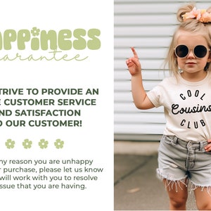 May include: A young girl wearing a white t-shirt with the text "COOL Cousins CLUB" in black. She is wearing denim shorts and has her hair pulled back with a pink bow. She is standing in front of a white slatted wall and pointing with her right hand. The text "happiness guarantee" is in green and white at the top of the image.