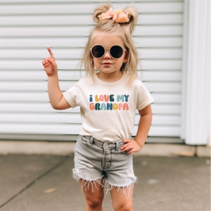 a little girl wearing a t - shirt that says i love my grandpa