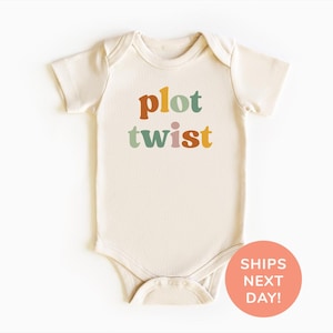 May include: A cream coloured baby onesie with the words "plot twist" printed in colourful letters. The letters are in a retro font style.