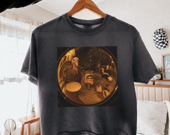 May include: A charcoal gray boxy crop t-shirt featuring a circular graphic print of a turkey, a raccoon, and a skunk gathered around food at night. The text BOXY CROP - PEPPER is printed in the upper right corner of the image above the shirt.