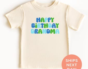 Könnte beinhalten: Cremefarbenes T-Shirt mit den Worten "HAPPY BIRTHDAY GRANDMA" in grünen, blauen und hellblauen Buchstaben. Ein runder, orangefarbener Aufkleber mit dem Text "SHIPS NEXT DAY!" befindet sich unten rechts.