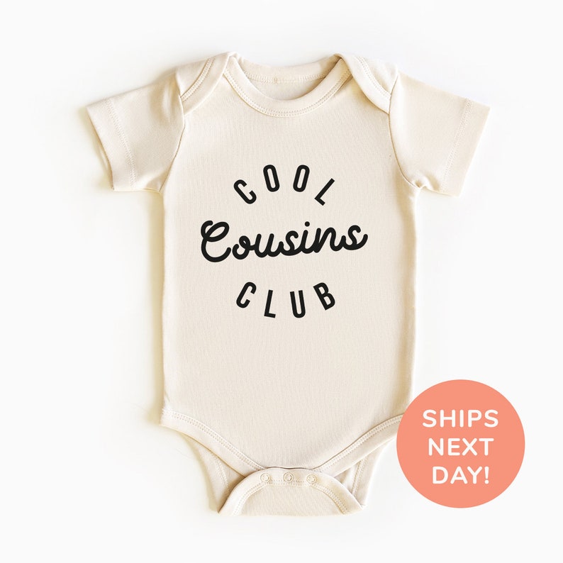 May include: A beige baby onesie with black text that reads "Cool Cousins Club" in a circle.