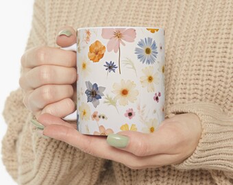May include: White ceramic mug with a floral pattern featuring various pressed flowers in shades of pink, yellow, blue, and orange.
