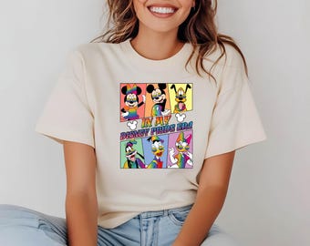 May include: A cream-colored t-shirt with a graphic of Disney characters wearing rainbow-colored glasses and the text "In My Disney Pride Era".